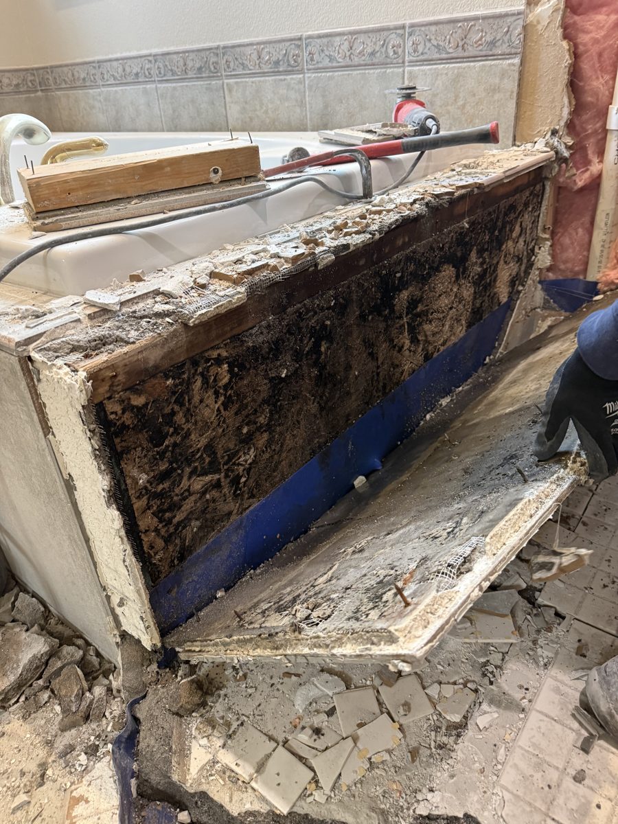Old tile tub deck opened up during a Colorado Springs bathroom remodel, showing crumbled, black-stained material under the tile