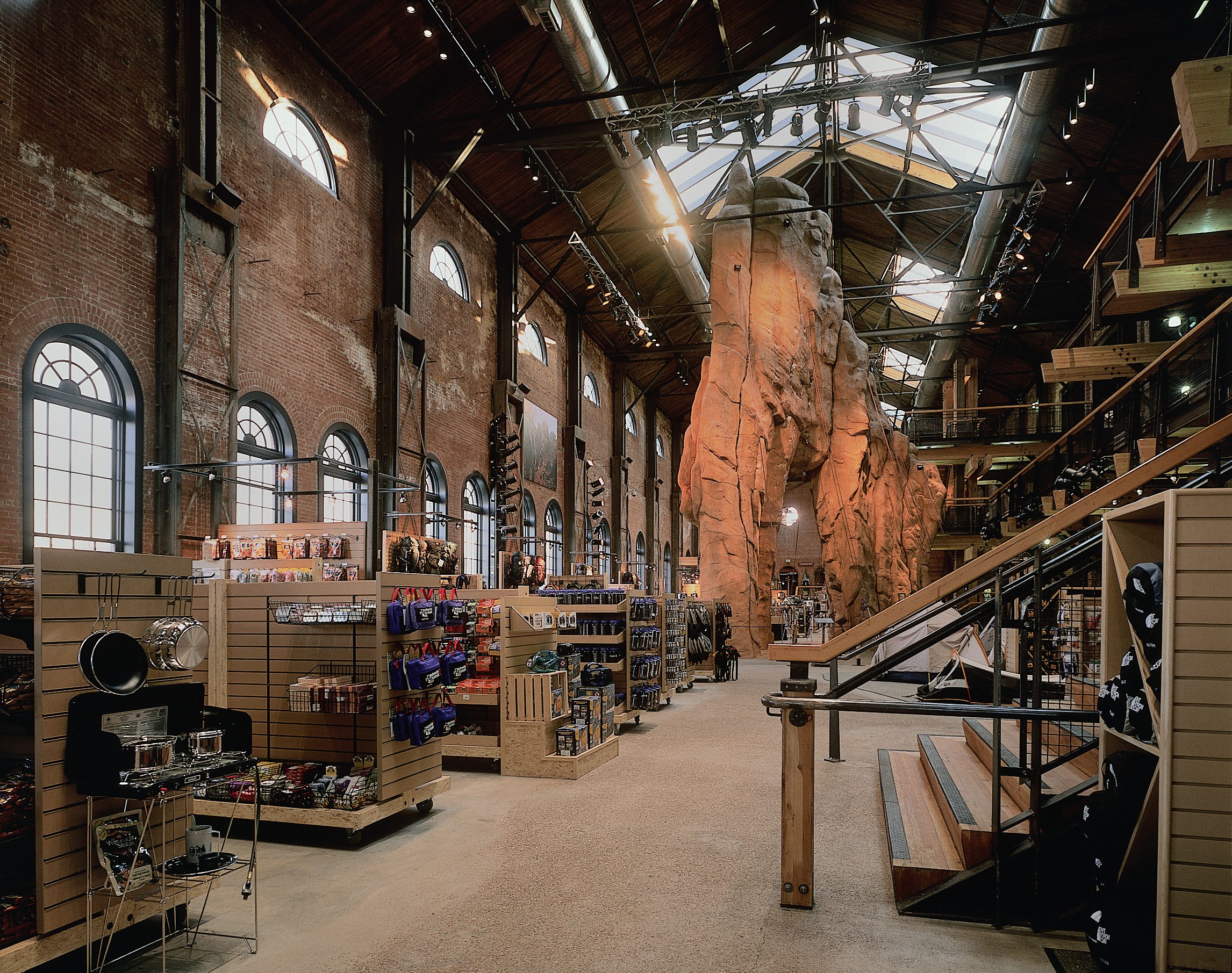 Inside the REI Denver flagship — the 35-foot climbing wall rising through the former turbine room, exposed brick and arched windows
