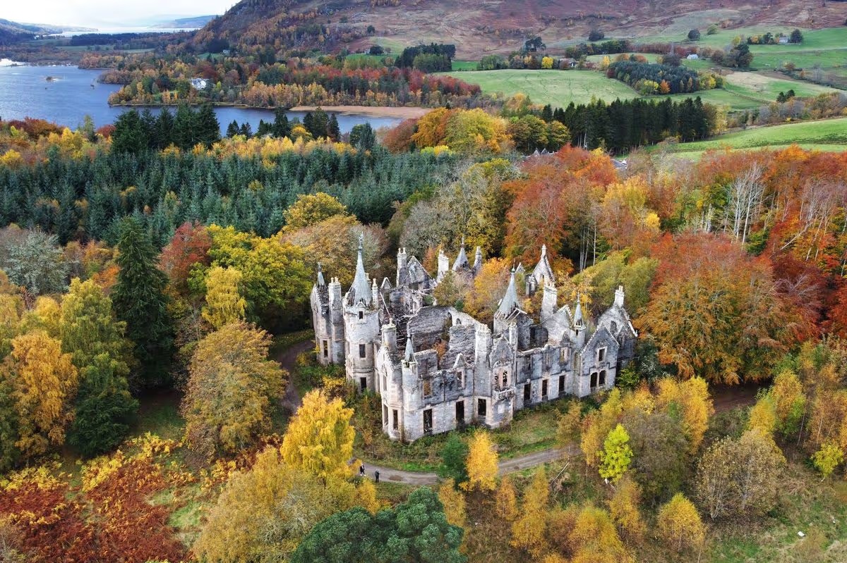 Aerial view of Dunalastair House, Perthshire, Scotland — roofless baronial mansion in autumn forest with a loch visible in the background