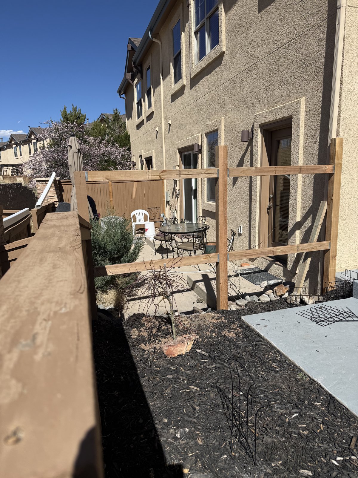 New fence posts and horizontal rails going up beside a stucco house, pickets not yet installed