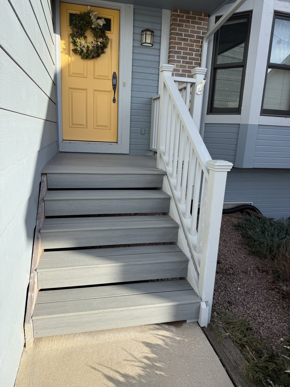 Finished gray composite front entry steps with a new white railing beside a yellow front door