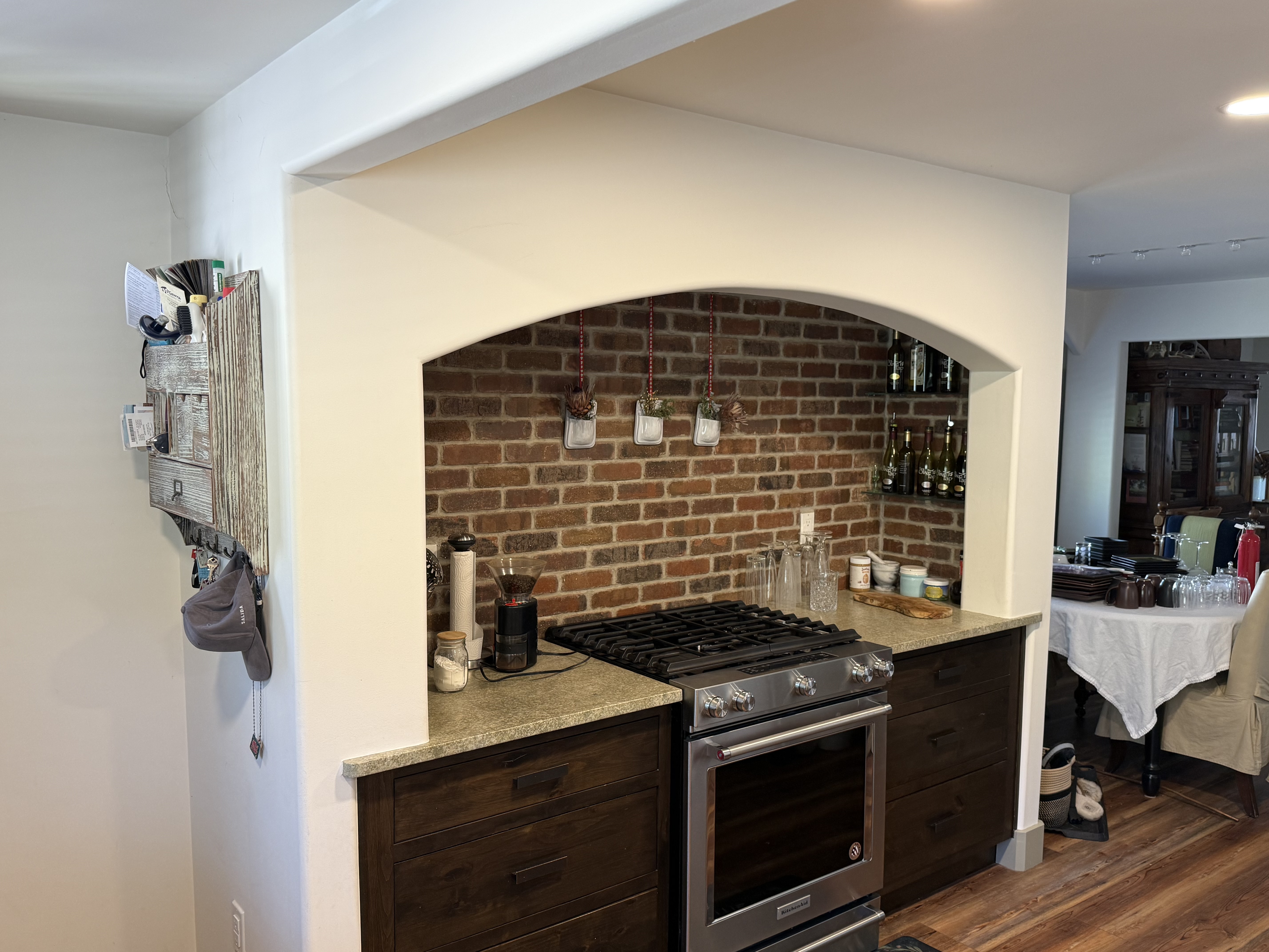 Finished kitchen with an arched alcove, exposed brick backsplash behind a stainless gas range, dark stained cabinets, and a speckled countertop