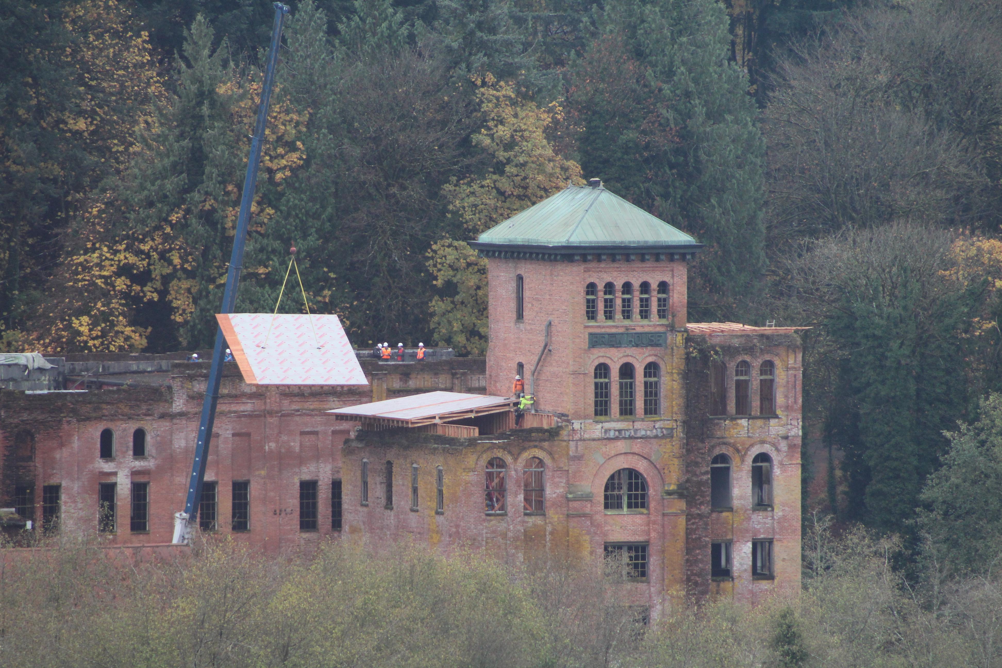 Active restoration of the Olympia Brewery tower — crane lifting a roof panel, workers on the roof, copper tower fully restored