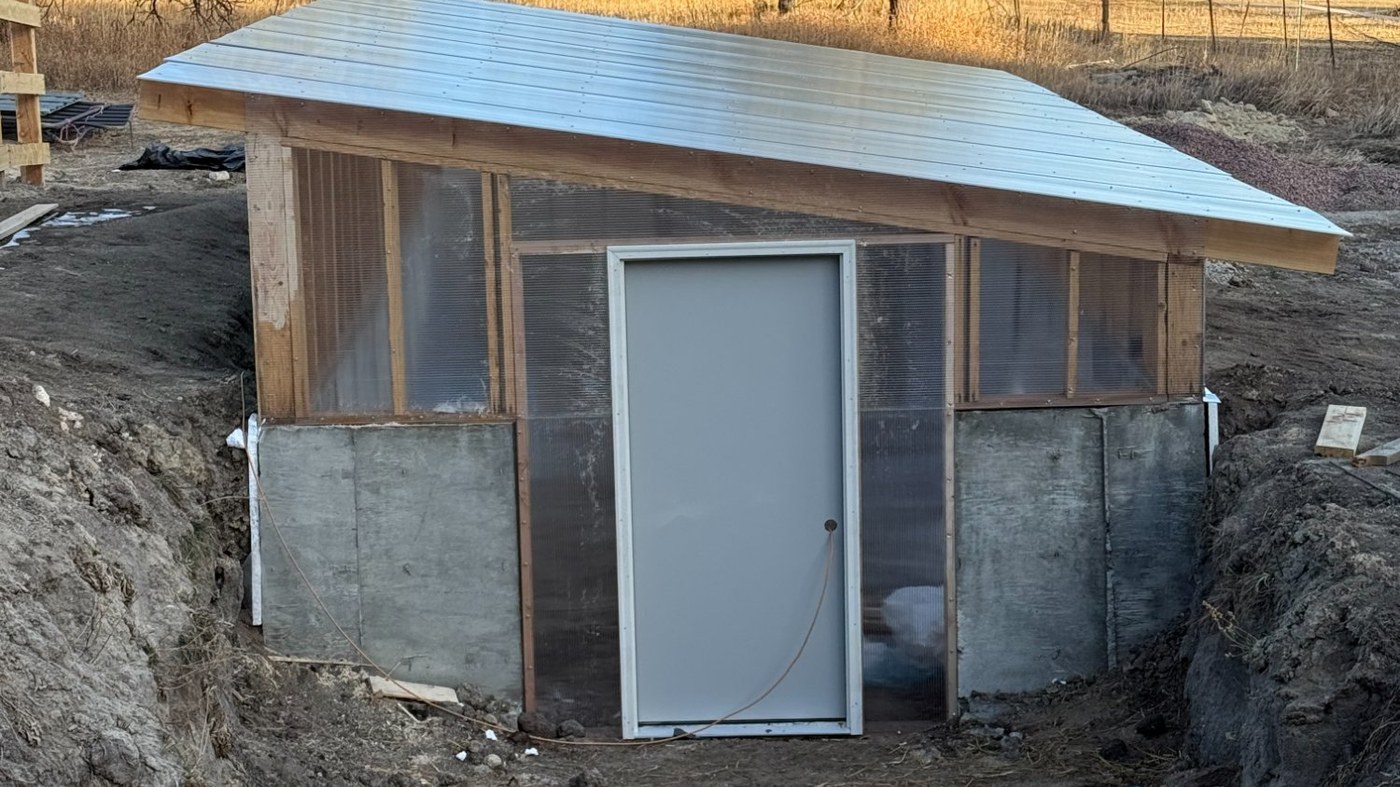 Completed Walpini sunken greenhouse built by The Colorado Handyman in Colorado Springs — set into the ground with polycarbonate glazing and ponderosa pines in the background